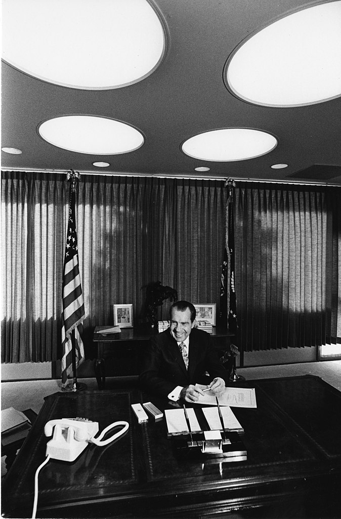 President Richard Nixon signs the National Environmental Policy Act (NEPA). A smiling Nixon sits behind a large desk flanked by flags.