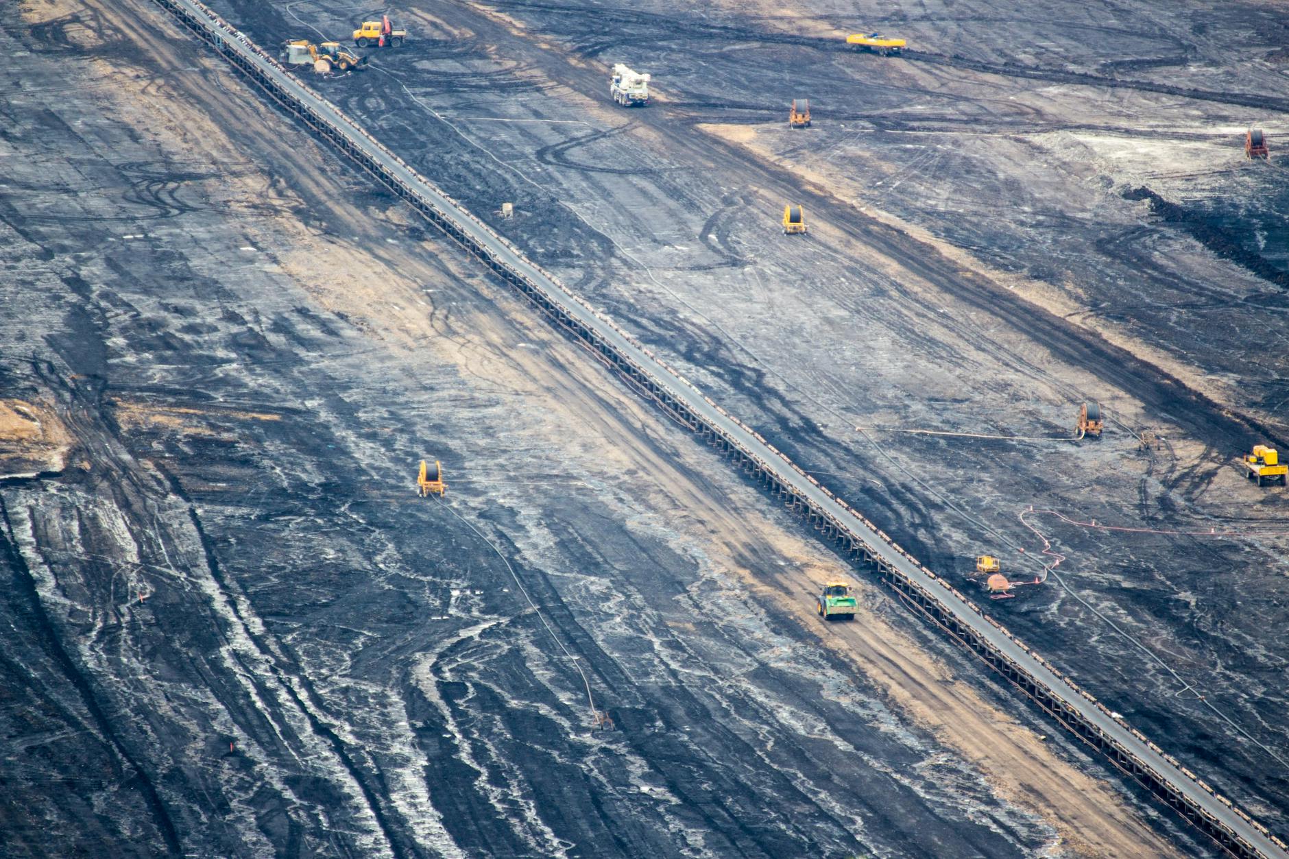 An aerial photo of mining. Multiple mining vehicles are dwarfed by the scale of the mine itself.